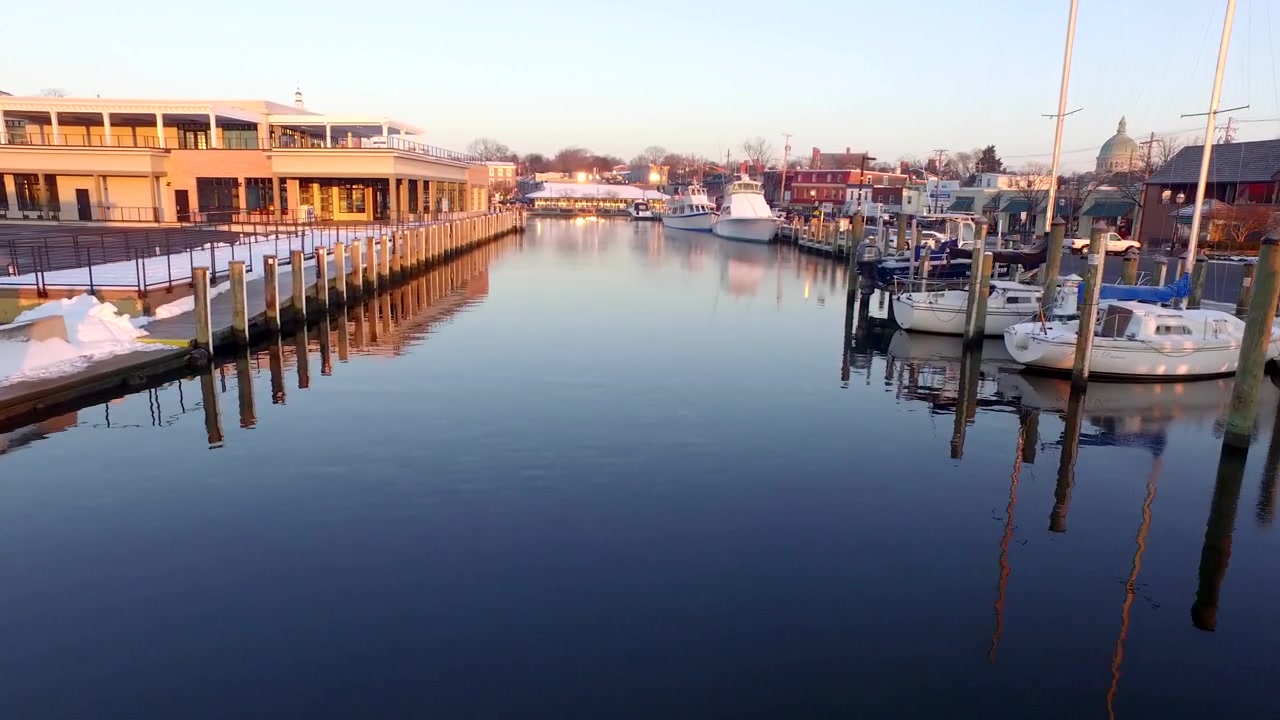 Medium aerial shot moving down Ego Alley in historic Annapolis Maryland during a golden winter sunrise. Snow on the boats.
