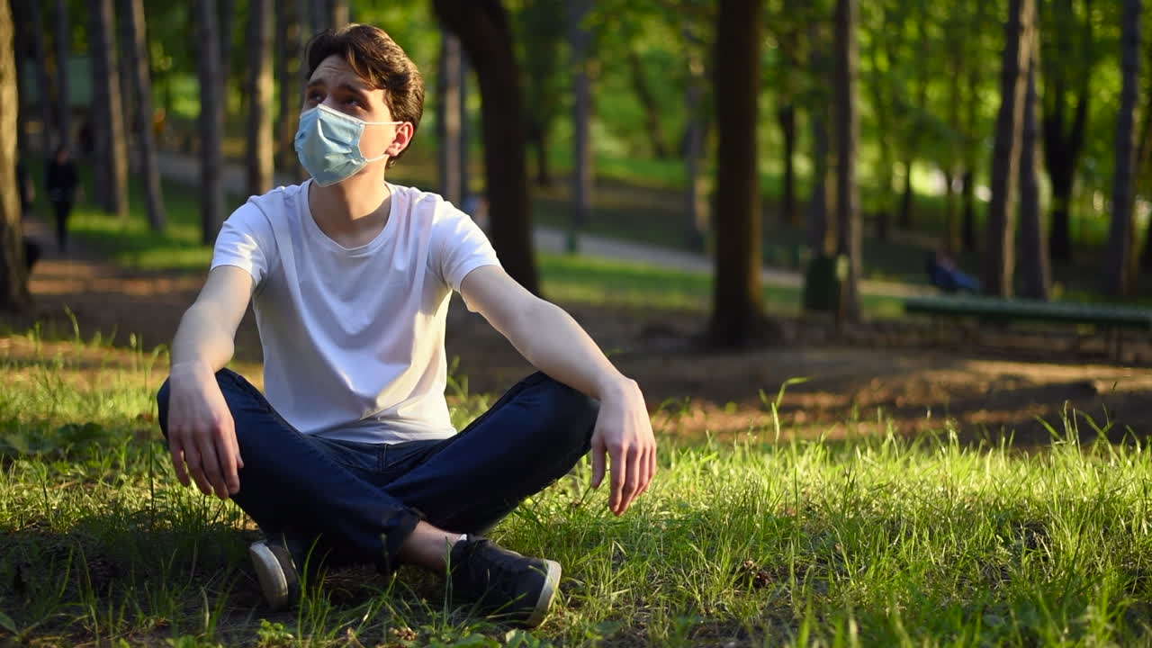 Young man in white t-shirt and a protective medical mask enjoying nature in the park. Sunny day. Corona Virus idea