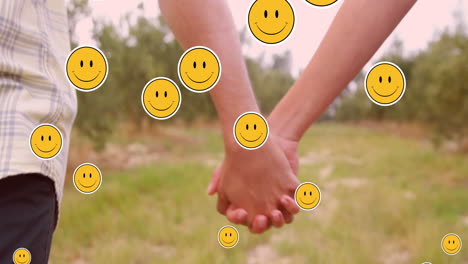 multiple smiling face emoji floating against mid section of couple holding hands