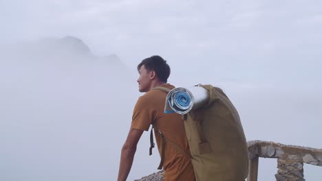 asian hiker male standing on a veranda cliff enjoys seeing beautiful view of top foggy mountain