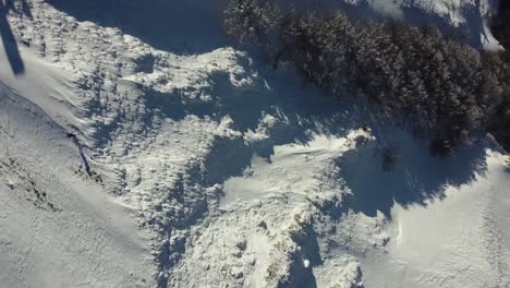 Aerial-top-down-of-winter-snow-covered-mountains-landscape-with-pine-tree-forest-hiking-trail-reach-top-peak-travel-destination