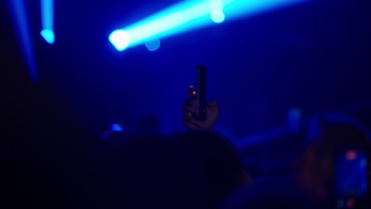 Il pubblico riprende un concerto dal vivo con smartphone sotto le luci intense del palco