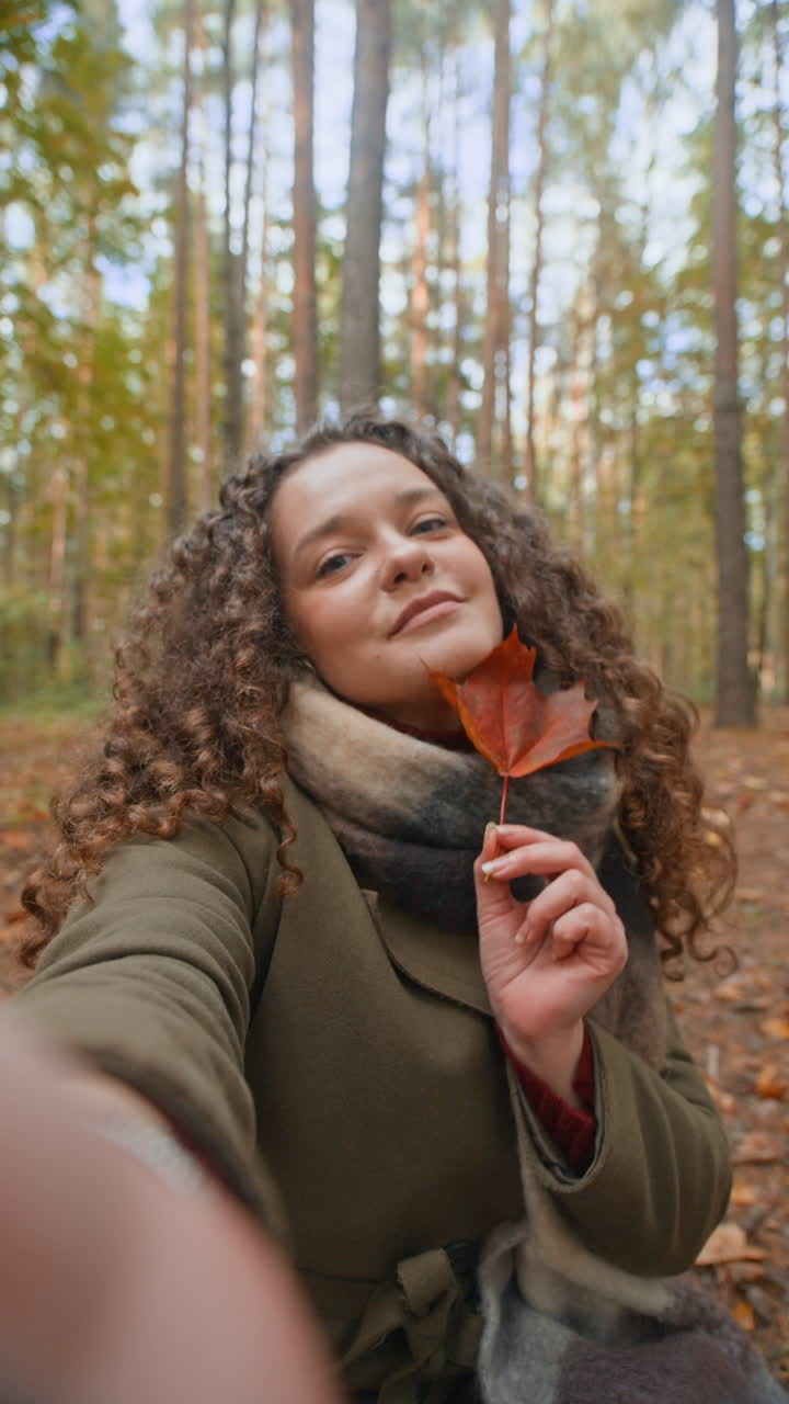 Woman with curly hair holding a leaf in the forest during autumn