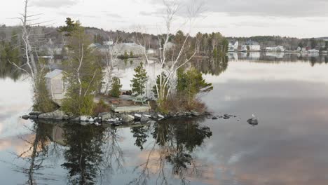 Tiny-sparse-island-with-a-small-shack-on-a-calm-lake-at-dusk-AERIAL-SLIDE