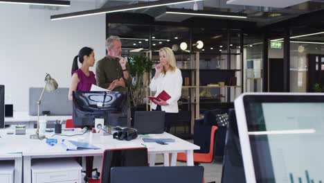 Diverse-business-colleagues-standing-using-computer-and-discussing-in-office