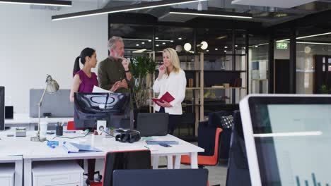 diverse business colleagues standing using computer and discussing in office