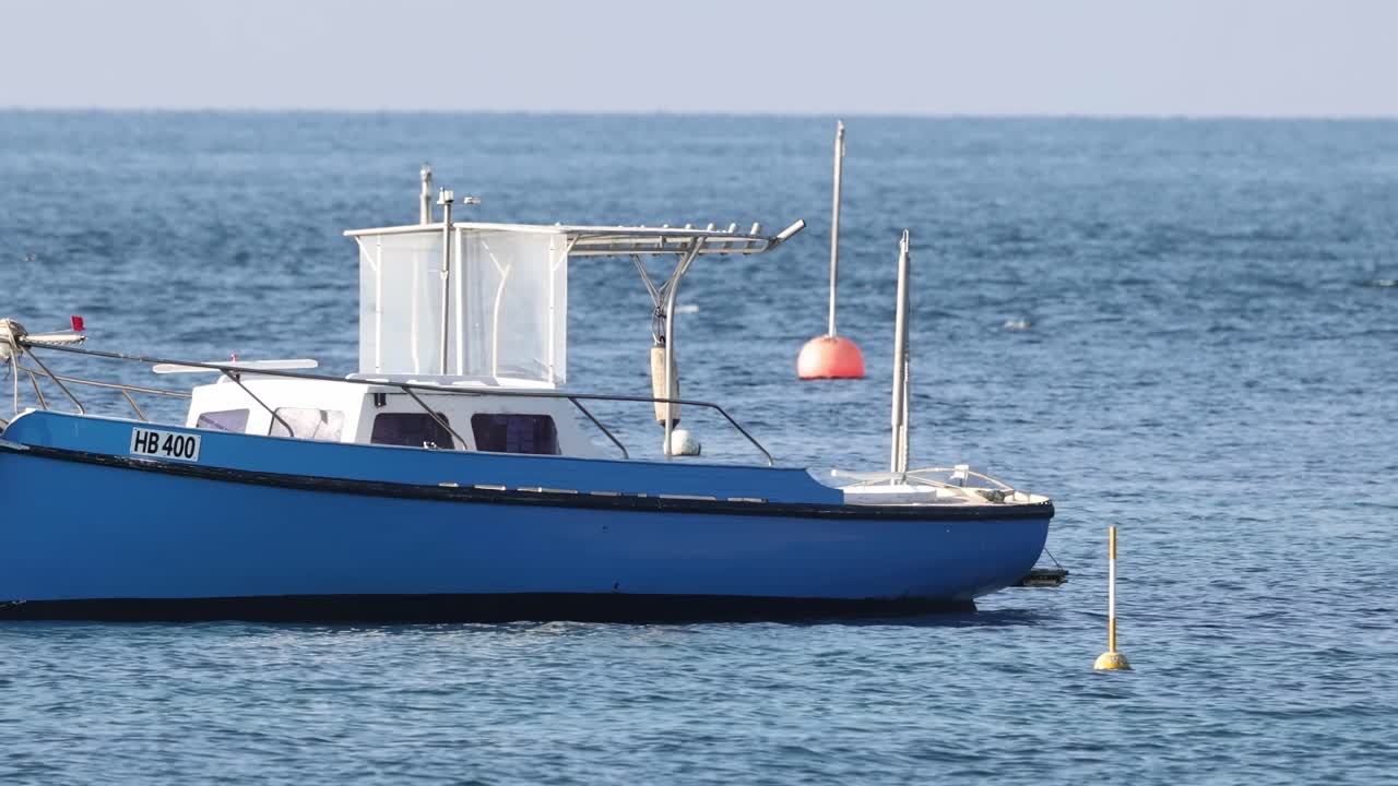 A blue boat is stationary in calm waters, positioned near red and yellow buoys.