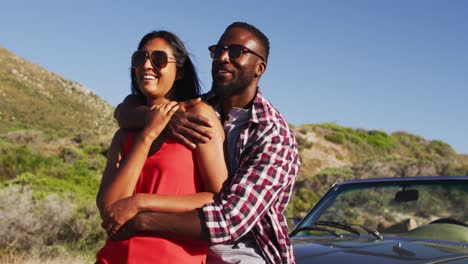 african american couple embracing each other while standing near convertible car on road
