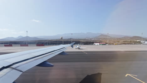 airplane wing on sunny runway with mountains in the background