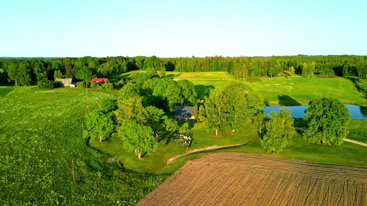 fotografía de un avión no tripulado orbital de una residencia rural entre campos verdes y árboles en el sol de verano, letonia