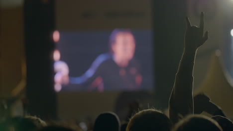 Spectator-man-showing-a-rock-devil-horns-gesture-in-front-of-big-screen-at-outdoor-music-concert