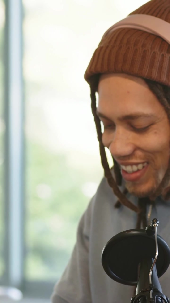 Vertical video: Adjusting mixer, man with beanie placing phones, talking to mic at desk, copy space