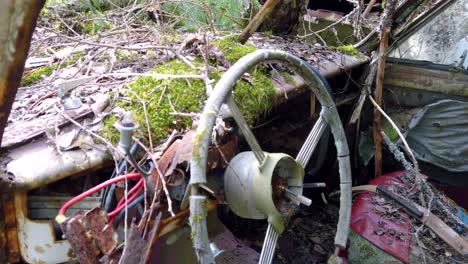 interior of old abandoned deteriorated vehicle with broken steering wheel, wires, moss growing on dashboard and falling to pieces, close up pan