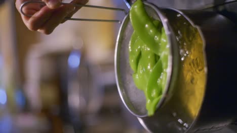 snow peas in strainer being drained of all water over boiling pot of broth, filmed as vertical closeup slow motion shot