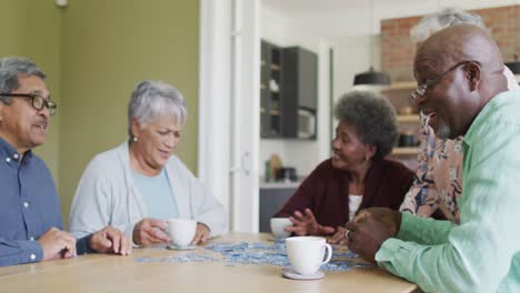 Gruppe-Glücklicher,-Vielfältiger-älterer-Freunde,-Die-Zu-Hause-Kaffee-Trinken-Und-Rätsel-Lösen