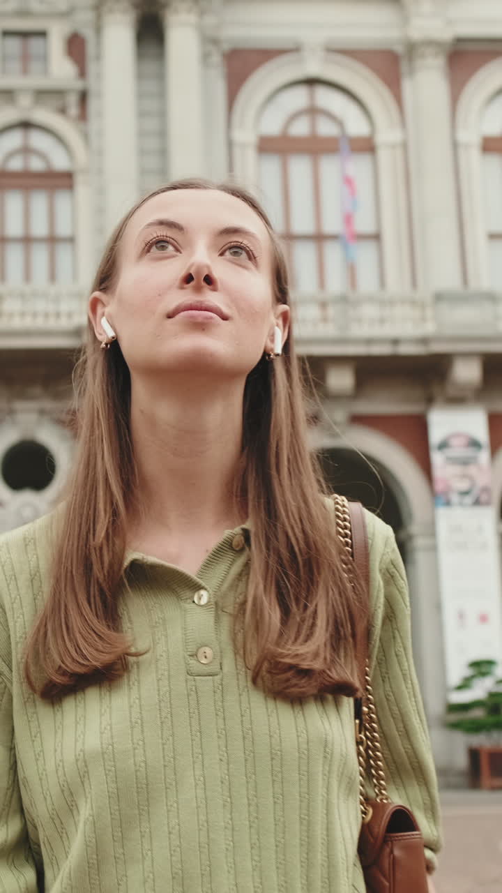 Giovane donna con auricolari che guarda in alto verso un edificio storico della città