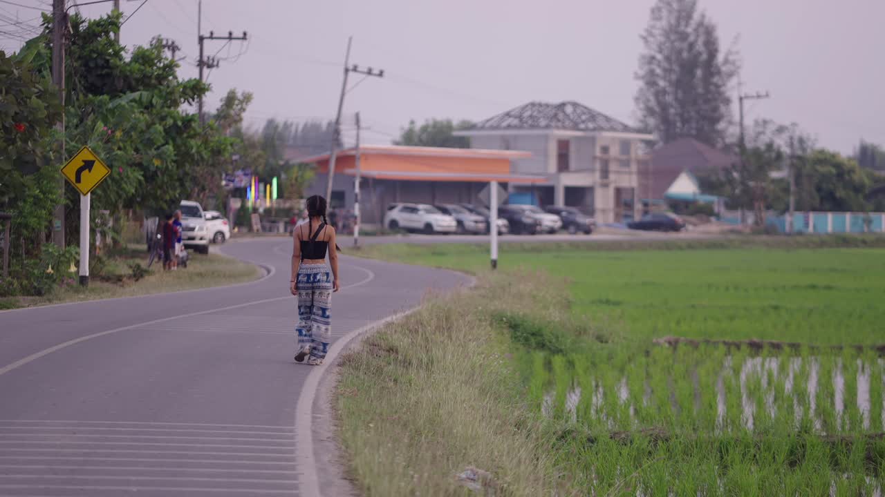 Person walking on a rural road next to a rice field