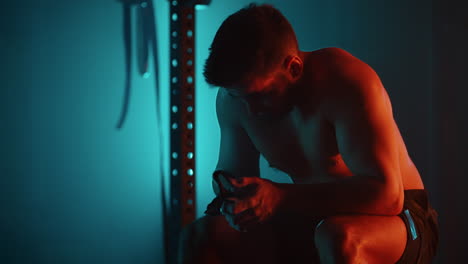 un hombre cansado después de un entrenamiento se sienta en una barra y descansa en el gimnasio en colores azul-naranja en cámara lenta