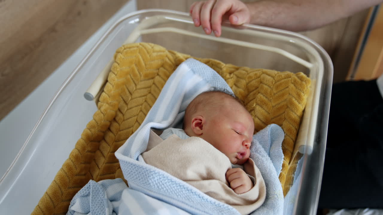 Lovely Caucasian baby sleeping in a crib. Unrecognized man sits near the cradle of his newborn child. Top view.