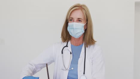 portrait of caucasian senior female doctor wearing surgical gloves and face mask using tablet comput