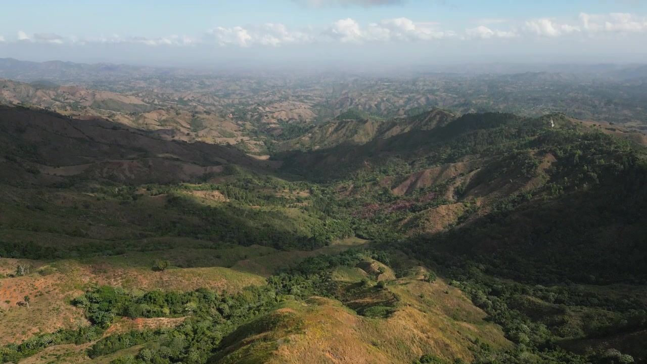 Drone aerial shot of the green hills and valleys in Constanza, Dominican Republic, under a clear blue sky