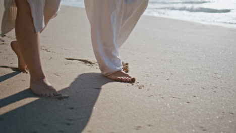 couple legs stepping sand beach leaving footprints closeup. pair tourist walking