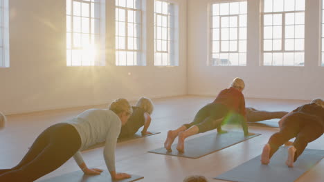 yoga class of mature old women practicing plank pose with instructor enjoying healthy lifestyle in studio at sunrise