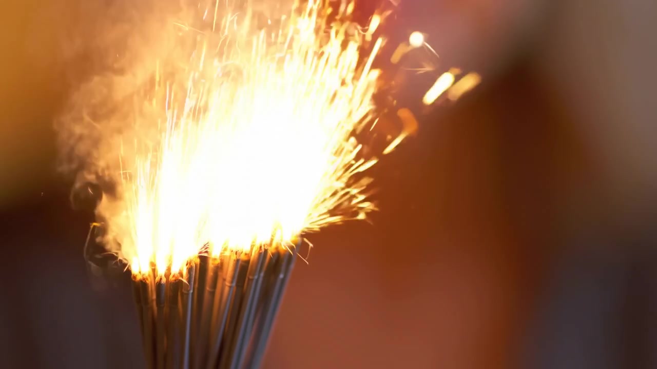 Nærbilde av brennende stjerneskudd, gnister flyr, kvinnehånd griper tynne metallstenger med lyse gylne flammer og glør