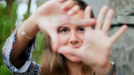 Beautiful-and-joyful-woman-frames-the-photographer-with-her-hands,-using-her-thumbs-and-index-fingers