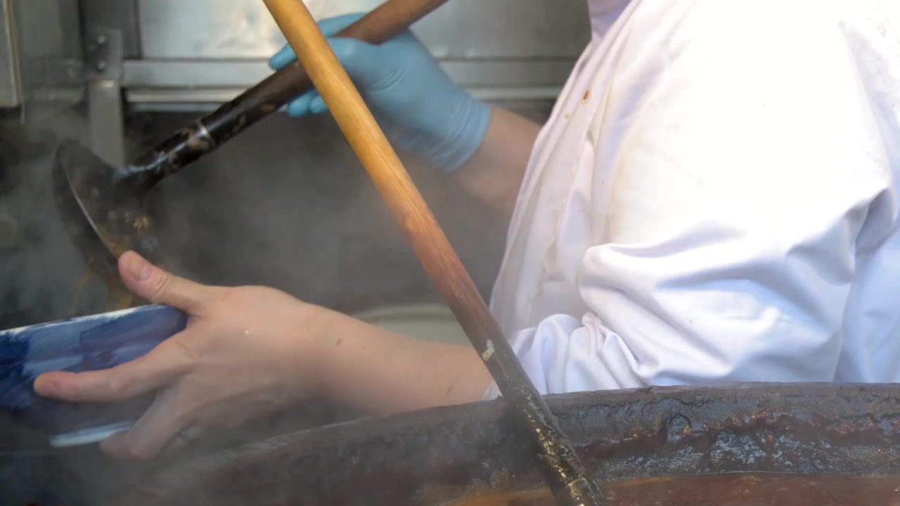Uno chef in uniforme bianca preleva stufato di miso caldo da una pentola fumante e lo versa in ciotole blu.