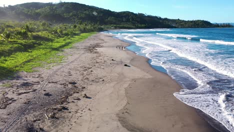 Aerial-drone-shot-of-individuals-alone-on-a-beach-during-sunset-with-clear-water-of-the-pacific-ocean