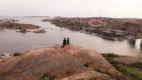 couple standing on a rocky hilltop overlooking a norwegian coastal village with their dog