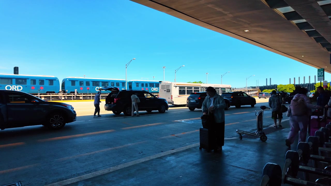 Chicago, AS, 9 Mei 2026: Wisatawan menunggu dengan bagasi di luar terminal bandara Chicago. Pemandangan tepi jalan menunjukkan penumpang, troli, mobil, dan bus carteran di bawah kanopi bangunan