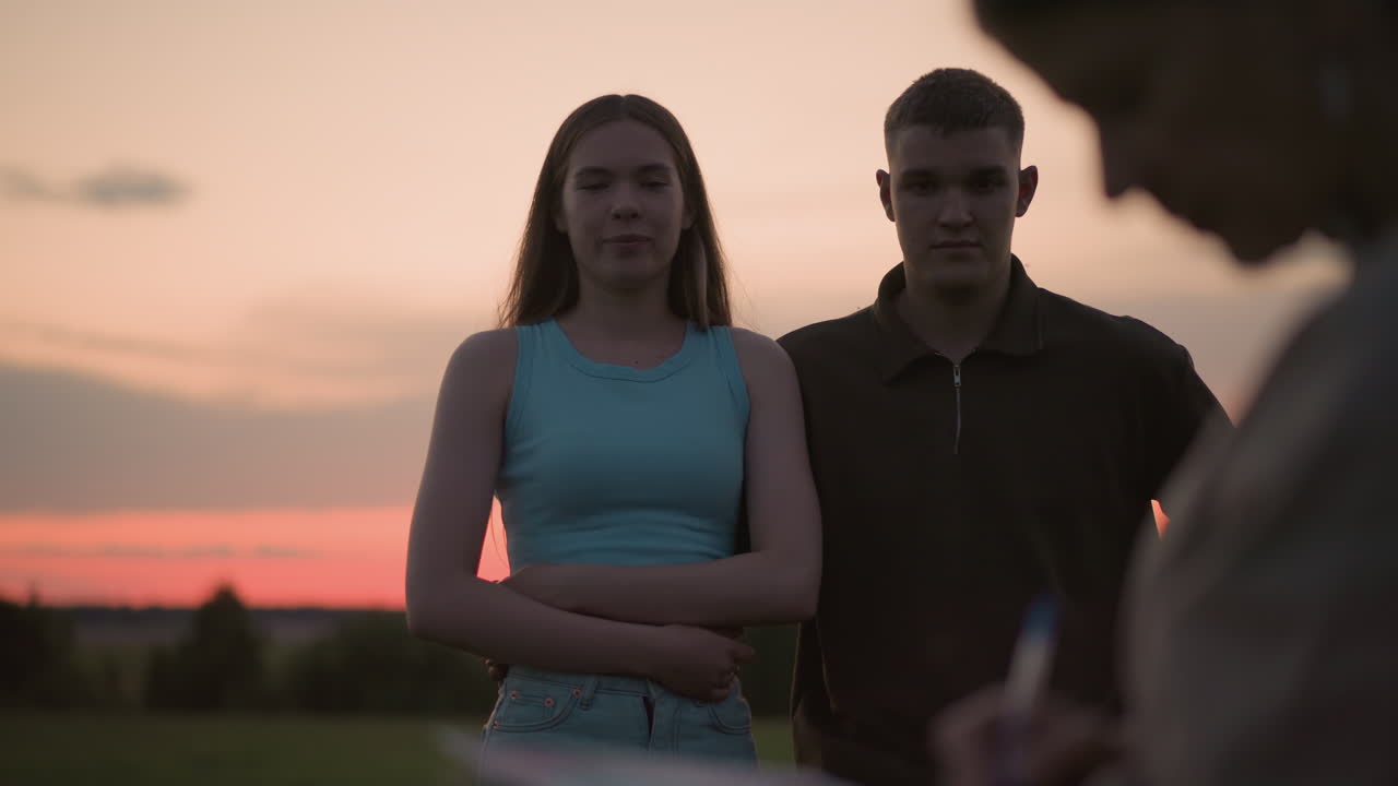 close blur view of person writing notes on surface while couple stands behind watching during sunset dusk sky with soft warm light and blurred landscape background