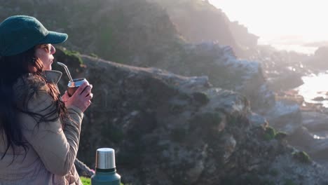 mujer bebiendo yerba mate, bebida típica argentina, en la playa, mientras observa la puesta de sol pichilemu, punta de lobos, playa para surfear, chile