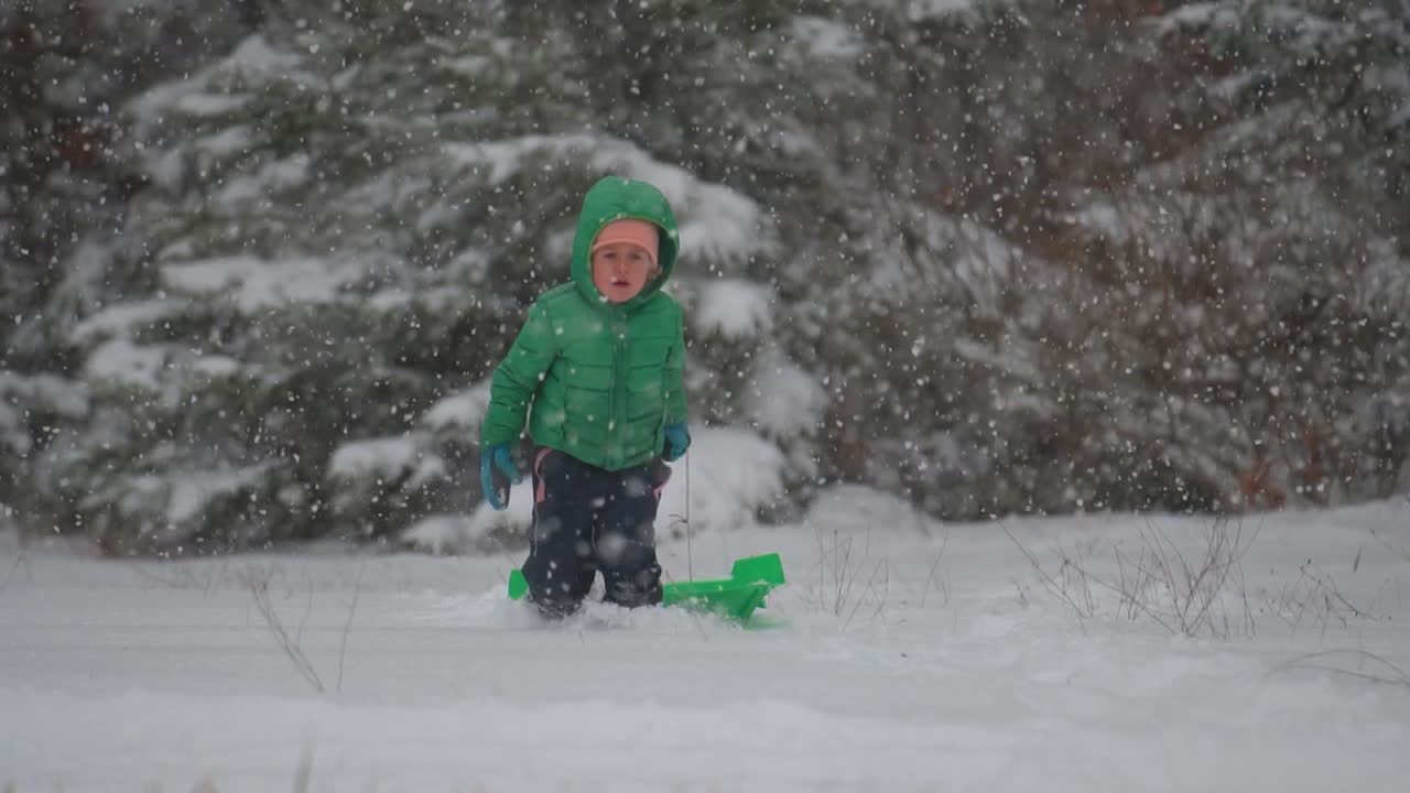 niño corriendo con trineo a través de la nieve mientras la nieve cae suavemente, cámara lenta