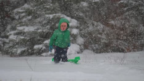 young boy running with sled through the snow while snow gently falls, slow motion