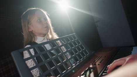 kid comprehends skill of singing with educator. little girl learner sharpens vocal skills with teacher in music studio against back light. musical training