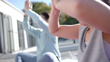 Happy-biracial-mother-and-daughter-practising-yoga-on-terrace-in-sunny-day,-slow-motion