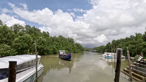 a speedboat travels along a calm mangrove river toward a wooden pier lined with boats under bright daylight, captured in a wide, steady shot