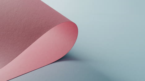 close up of pink rolled piece of paper on pale blue background with copy space in slow motion