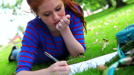 Pretty-young-student-lying-on-the-grass-studying