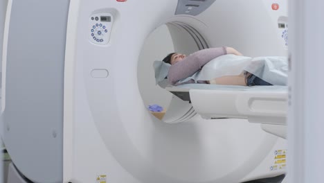 mujer acostada en el escáner de ct o mri durante la máquina de imágenes de su cuerpo, se enciende los rayos infrarrojos y la paciente pasa a través del círculo, grúa disparada de abajo hacia arriba, interior de la habitación, escena activa.