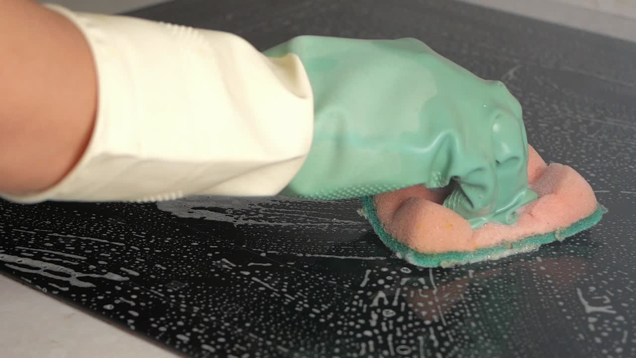 Hand in Glove Cleaning Soapy Black Kitchen Surface with Sponge