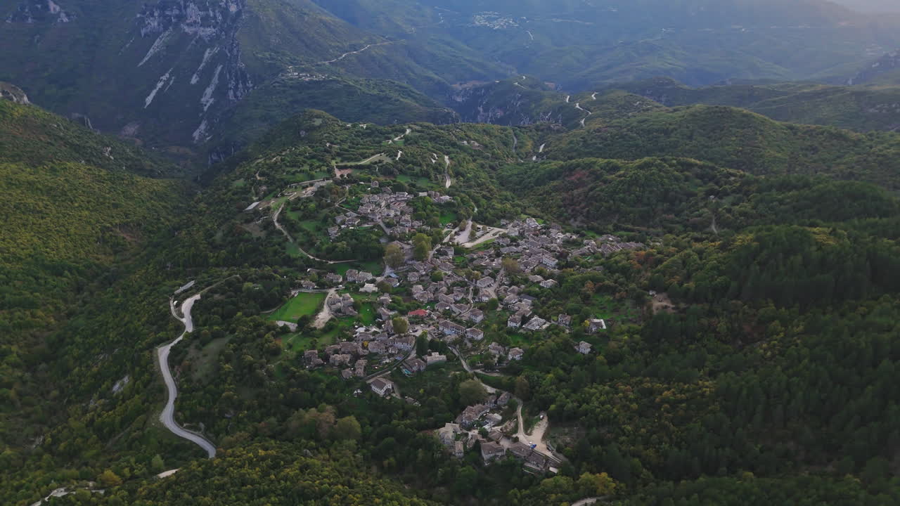Aerial establishing view of Papigo village nestled in lush green Zagori landscape, surrounded by mountains