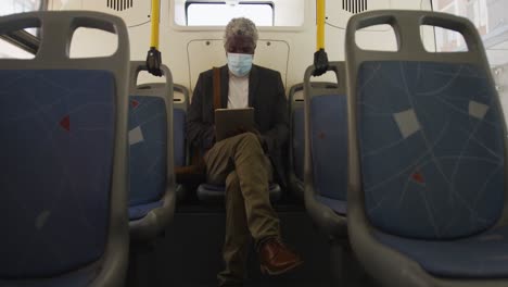 African-american-senior-man-wearing-face-mask-using-digital-tablet-while-sitting-in-the-bus