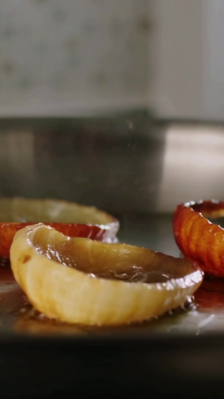 Vertical video: Sizzling fruit rings browning under burner heat on home stove in metal pan to glaze