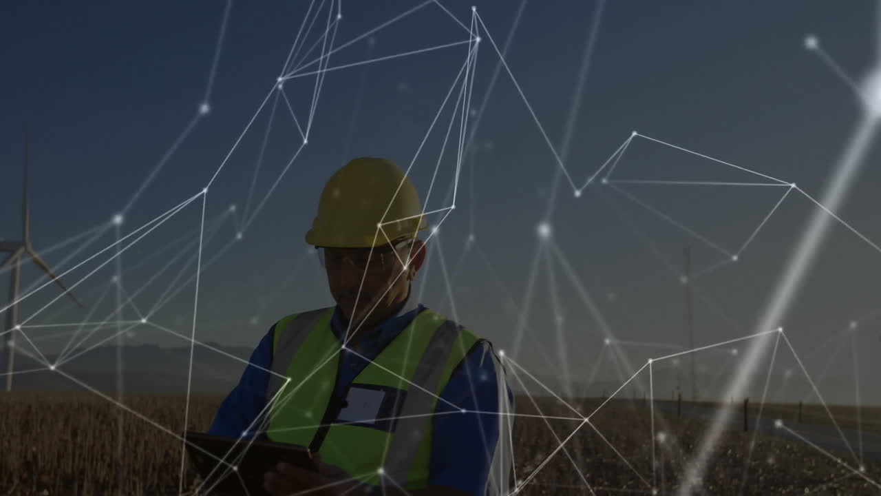 Engineer wearing safety vest monitoring wind farm data on tablet overlaid with network graphics