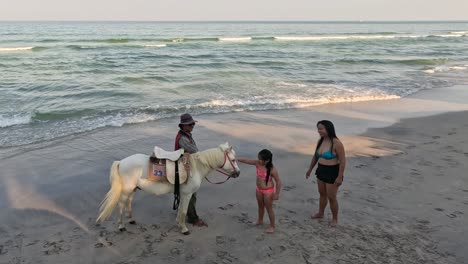 horse handler offers ride to mother and child on beach