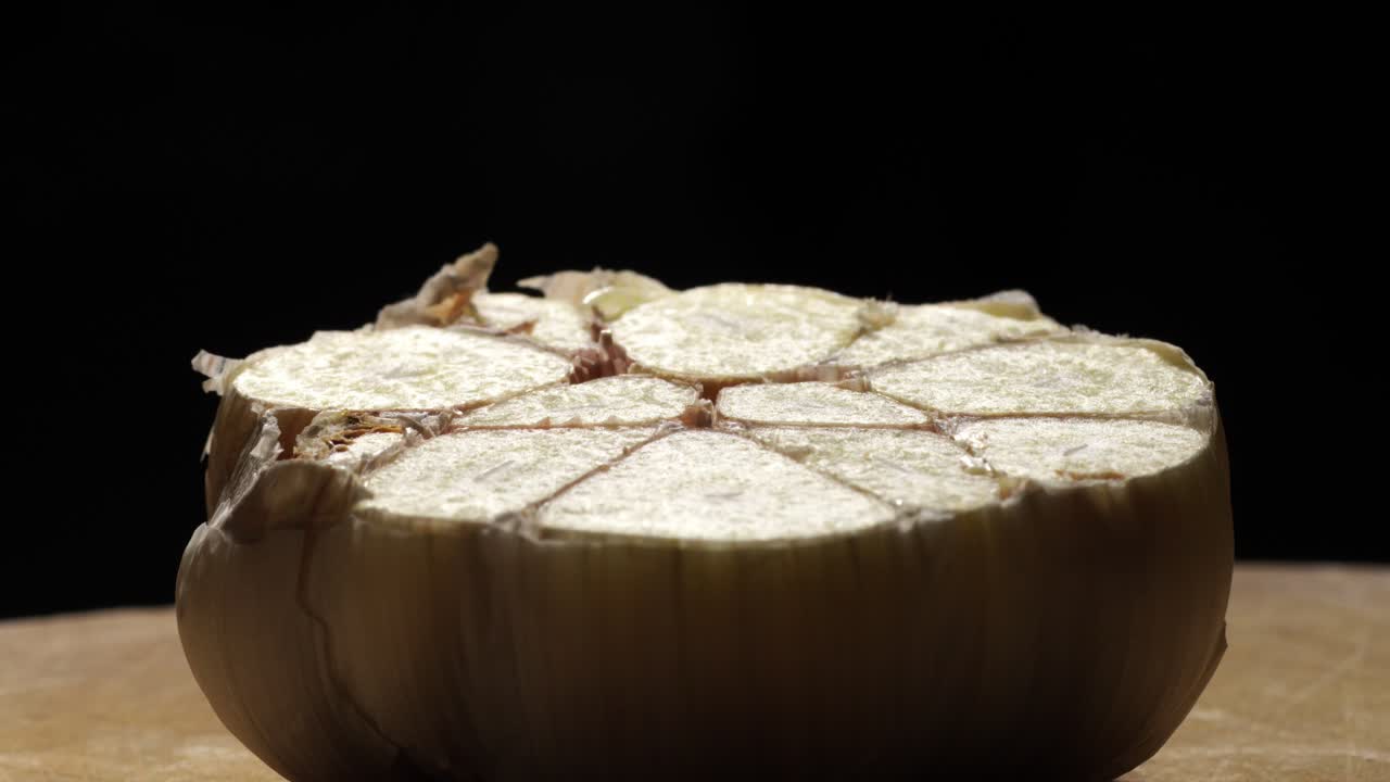 Close-up of sliced garlic head on wooden board with dark background